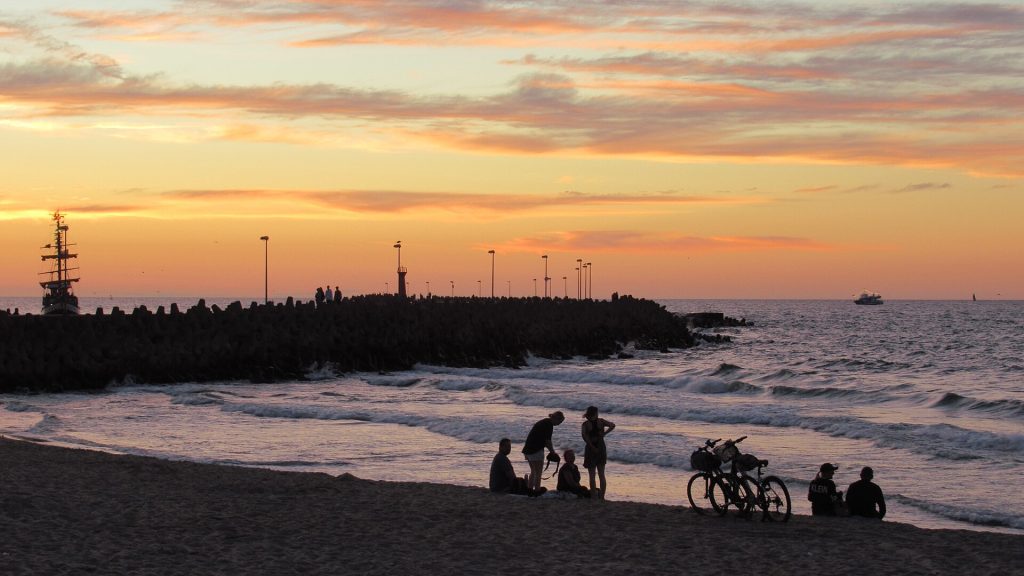 ludzie z rowerami na plaży przy falochronie w Kołobrzegu o zachodzie słońca